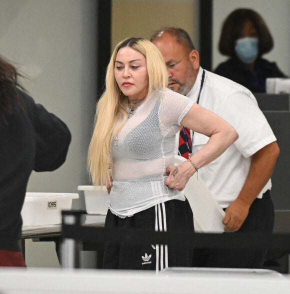 Madonna et son fils David Banda, 16 ans, arrivent à l'aéroport JFK à New York, le 11 août 2022. Au moment de passer le contrôle avant d'embarquer, la chanteuse de 63 ans laisse apparaître son tee-shirt en résille transparent.