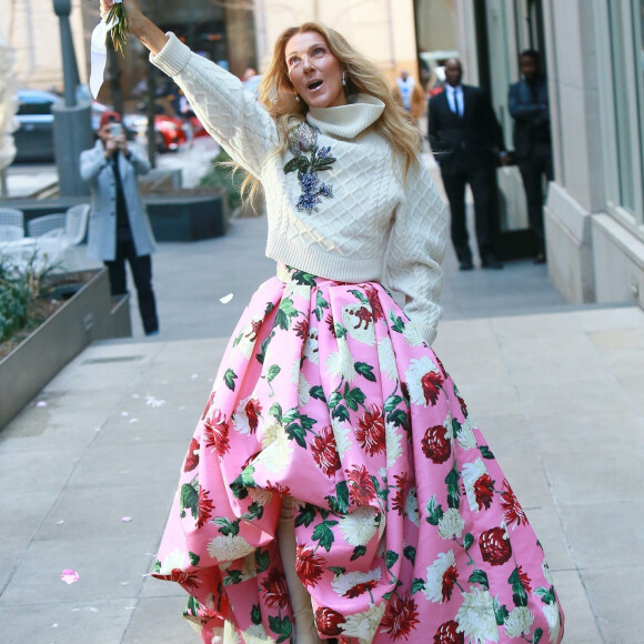 Celine Dion rayonnante et très souriante dans un ensemble pull écru et jupe bouffante fleurie salue ses fans à la sortie de son hôtel à New York, le 8 mars 2020 