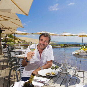 Bernard Montiel, présentateur et animateur radio pose sur la terrasse du restaurant "La Corniche" en dégustant un verre de vin blanc du château Smith Au Lafitte et quelques huïtres. . La Teste-de-Buch Pyla-Sur-Mer, le 14 juillet 2017. © Thibaud Moritz / Bestimage