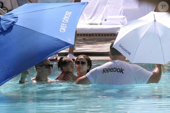 Jennifer Lopez et Casper Smart, dans la piscine avec Emme, tentent de se protéger des photographes à l'aide de parasols. Miami, le 30 août 2012.