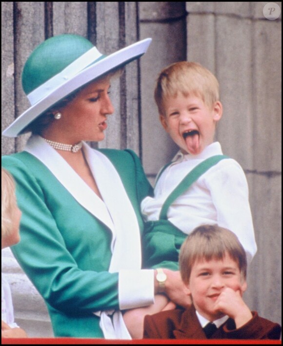 Le prince Harry fait son malicieux dans les bras de la princesse Diana et dans le dos du prince William, le 12 juin 1988 pendant la parade Trooping the Colour.