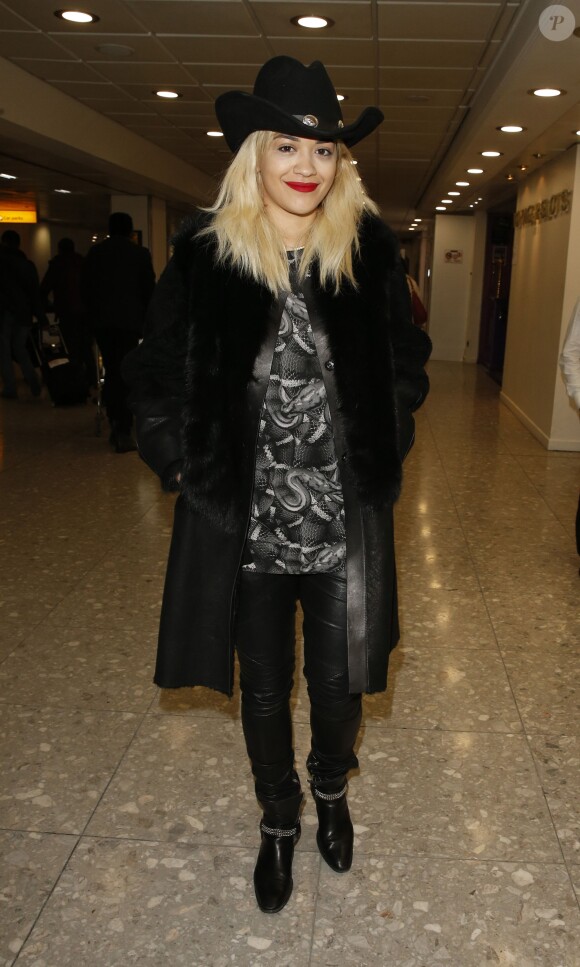 Rita Ora, à l'aéroporth d'Heathrow à Londres, habillée d'un t-shirt County of Milan, d'un pantalon en cuir Balmain et de bottines Saint Laurent. Le 15 février 2014.