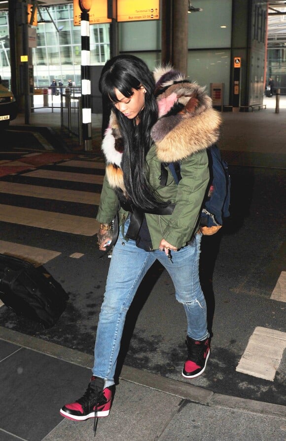 Rihanna arrive à l'aéroport d'Heathrow à Londres, habillée d'une parka Mr and Mrs, de baskets Nike Air Jordan I et d'un sac à dos oversize Adam Selman. Le 24 mars 2014.