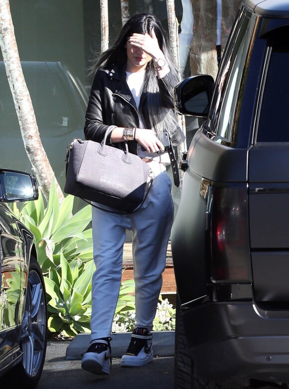 Kylie Jenner quitte le salon de coiffure Andy LeCompte à West Hollywood, habillée d'une veste en cuir noire, d'un ensemble blanc et de baskets Nike + R.T. (modèle Nike Air Force 1 revisité par Riccardo Tisci). Un sac gris Givenchy (modèle Antigona) complète sa tenue. Le 3 novembre 2014.