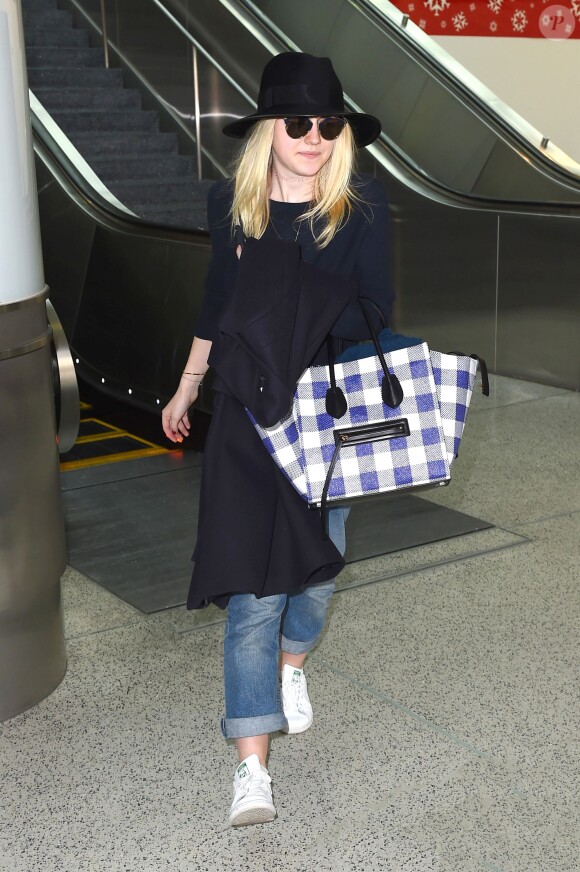 Dakota Fanning arrive à l'aéroport LAX de Los Angeles, et porte un sac à carreaux Céline (modèle Phantom), un jean "boyfriend" et des baskets adidas Originals (modèle Stan Smith). Le 19 décembre 2014.