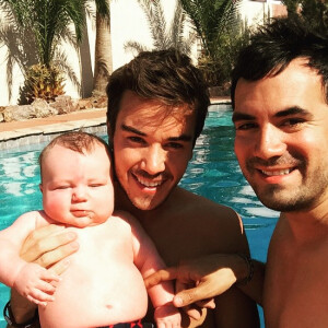 Alex Goude, Romain et leur bébé Elliot posent ensemble dans la piscine. Juin 2015.