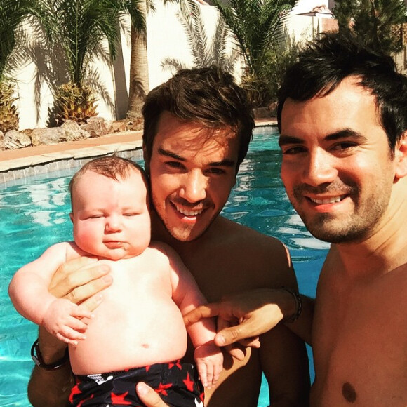 Alex Goude, Romain et leur bébé Elliot posent ensemble dans la piscine. Juin 2015.