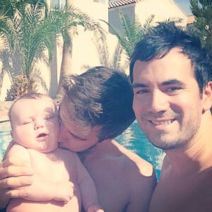 L'animateur Alex Goude, Romain et leur bébé Elliot posent ensemble dans la piscine. Juin 2015.