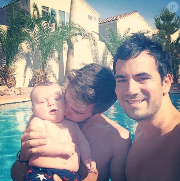 L'animateur Alex Goude, Romain et leur bébé Elliot posent ensemble dans la piscine. Juin 2015.