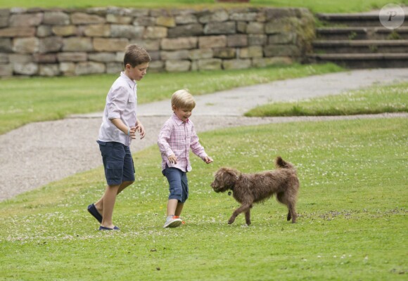 Le prince Christian et le prince Vincent joue avec un des chiens de la famille. La famille royale de Danemark posait le 25 juillet 2015 dans le parc du château de Grastenpour la traditionnelle séance photo des vacances d'été.