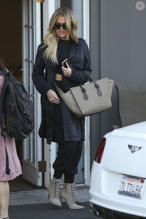 Khloé Kardashian quitte un studio de tournage à Los Angeles, habillée d'un tranch-coat, d'un crop top et d'un pantalon noirs. Des lunettes de soleil Porsche Design, un sac Céline et des bottines Balmain complètent sa tenue. Le 11 août 2015.