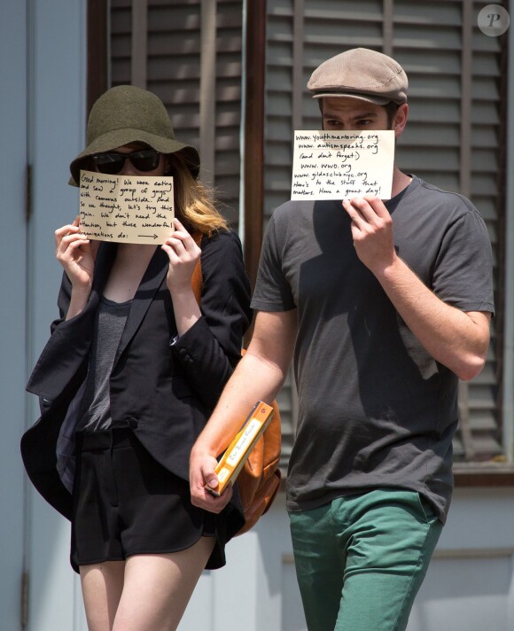 Emma Stone et son petit-ami Andrew Garfield se cachent le visage avec chacun un message en sortant d'un déjeuner au Cafe Cluny à New York, le 17 juin 2014. Sur leurs papiers on peut lire qu'ils n'ont pas besoin de publicité mais que les associations mentionnées en ont vraiment besoin.