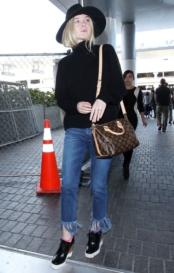 Elle Fanning à l'aéroport LAX de Los Angeles, porte un chapeau et un pull à col roulé noirs, un sac Louis Vuitton (modèle Speedy Bandoulière), un jean 3x1 et des chaussures Stella McCartney. Le 4 novembre 2015.