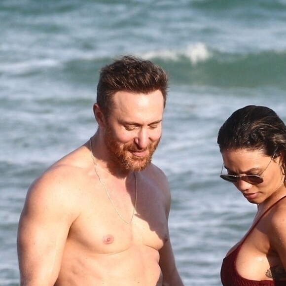 David Guetta et sa compagne Jessica Ledon, qui arbore un diamant à l'annulaire gauche, passent du bon temps sur la plage en compagnie de leur petit chien. Miami, le 23 novembre 2018. 