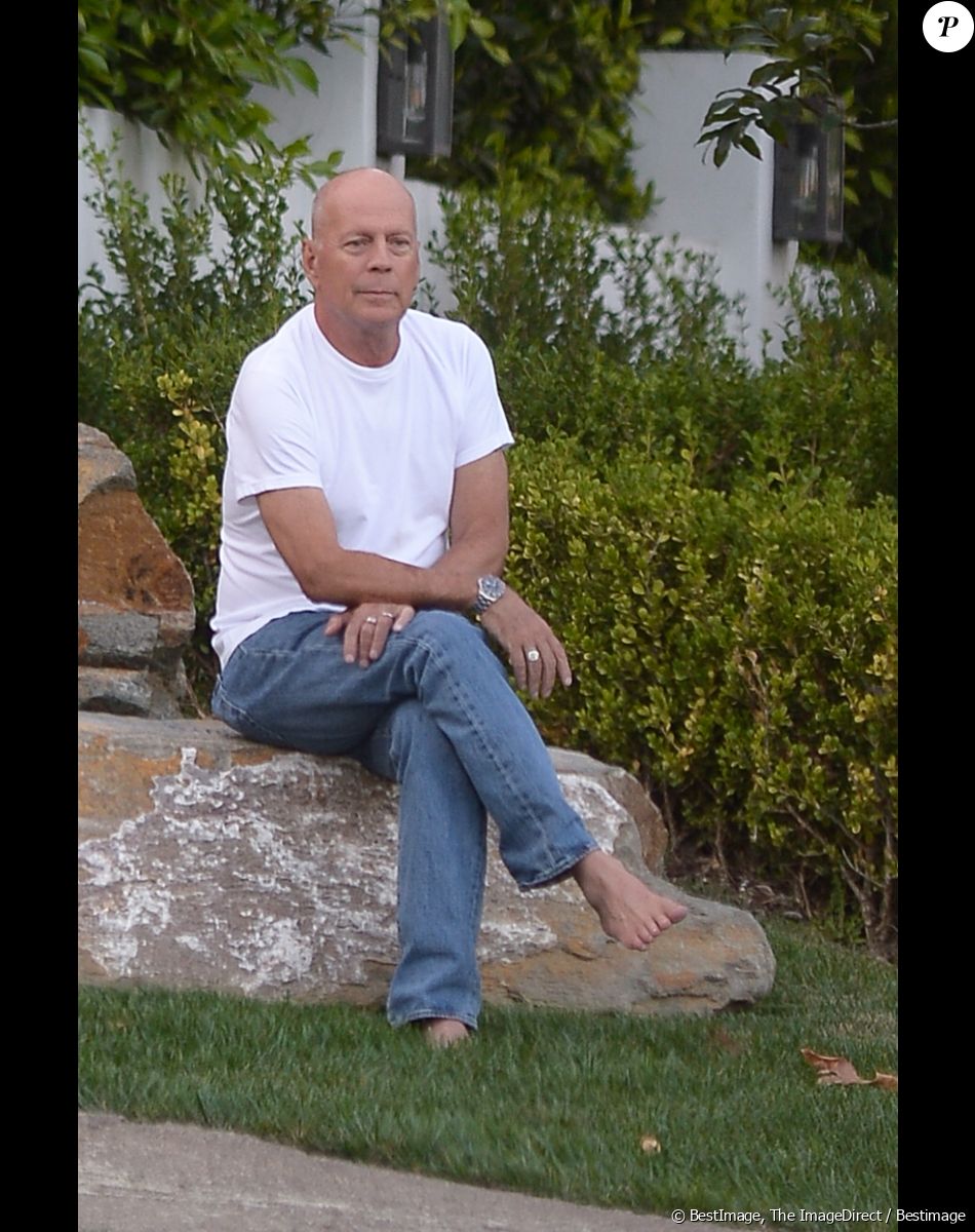 Exclusif - Bruce Willis est assis pieds nus sur un rocher et regarde passer les voitures sur Sunset Boulevard à Los Angeles, le 22 septembre 2019. Il porte un jean et un t-shirt blanc.