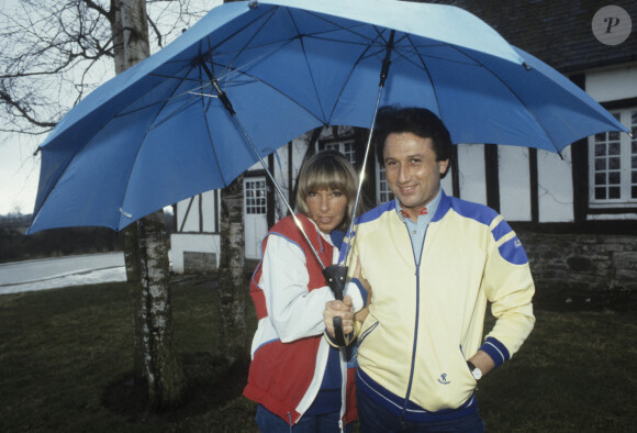 En France, Michel Drucker, avec sa femme Dany Saval, se promenant dans le jardin et s'abritant sous des parapluies © Michel Ristroph via Bestimage