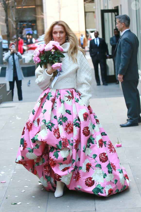 Celine Dion rayonnante et très souriante dans un ensemble pull écru et jupe bouffante fleurie salue ses fans à la sortie de son hôtel à New York, le 8 mars 2020 