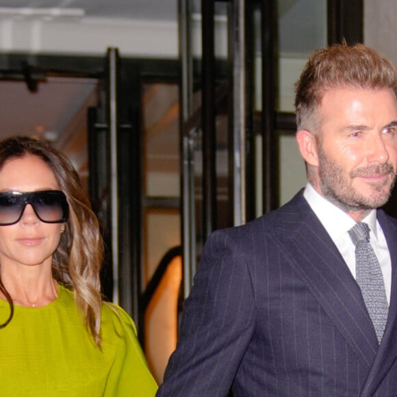Victoria et David Beckham se tiennent la main à la sortie de leur hôtel à New York le 14 octobre 2022. Victoria porte une robe verte électrique et David un costume bleu marine.