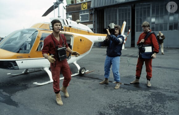 Archives - En France, Philippe de Dieuleveult, devant l'hélicoptère, vêtu de sa combinaison rouge, portant son casque d'écoute et son poste émetteur, le cameraman, Patrick FABRY et le responsable du magnétoscope, Serge BEAUPERE lors de l'émission La chasse aux trésors en mai 1983