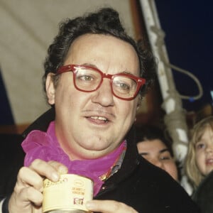 Archives - En France, à Genevilliers, sous le chapiteau des Restaurants du coeur, lors d'une distribution de nourriture, entouré de bénévoles, Coluche arborant un badge de l'association sur son blouson le 3 janvier 1986.