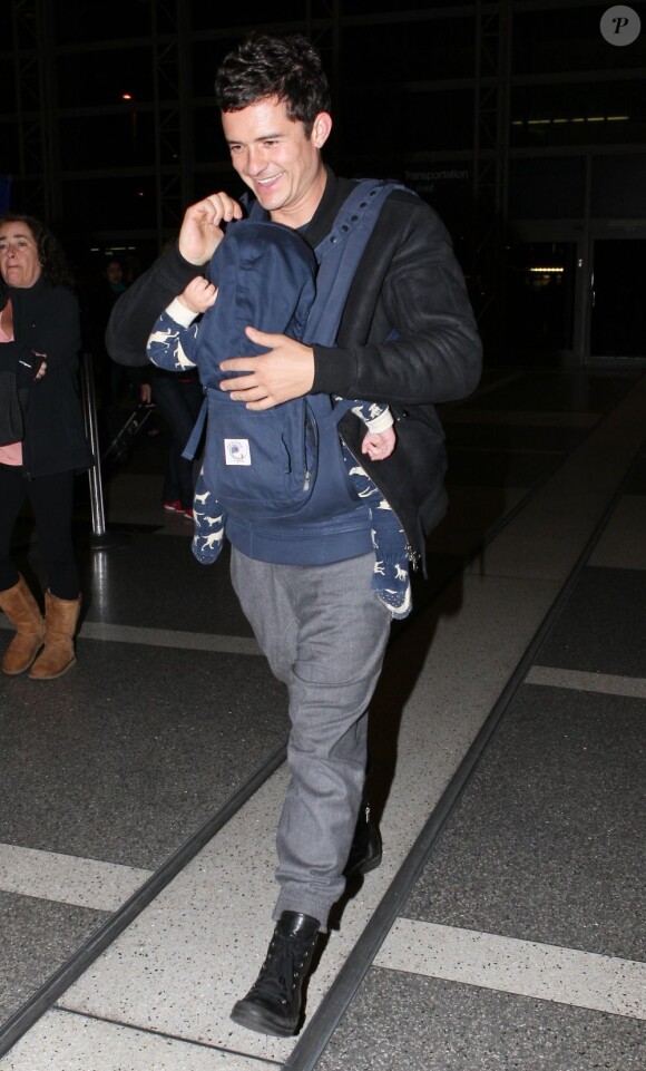Orlando Bloom souriant en compagnie de son fils Flynn à l'aéroport de Los Angeles le 13 avril 2012