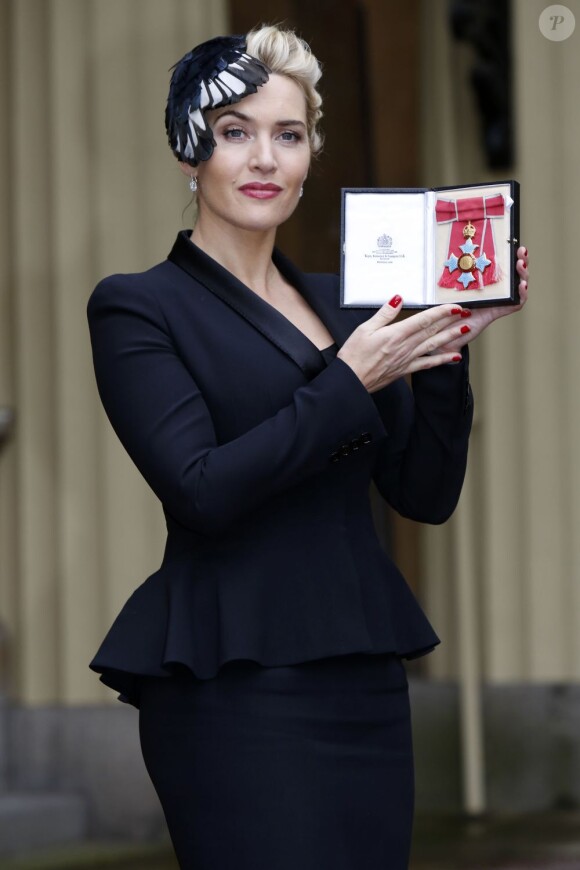 Kate Winslet, droite et magnifique avec son tailleur noir, avec son insigne de Commandant dans l'Ordre de l'Empire Britannique, le 21 novembre 2012.