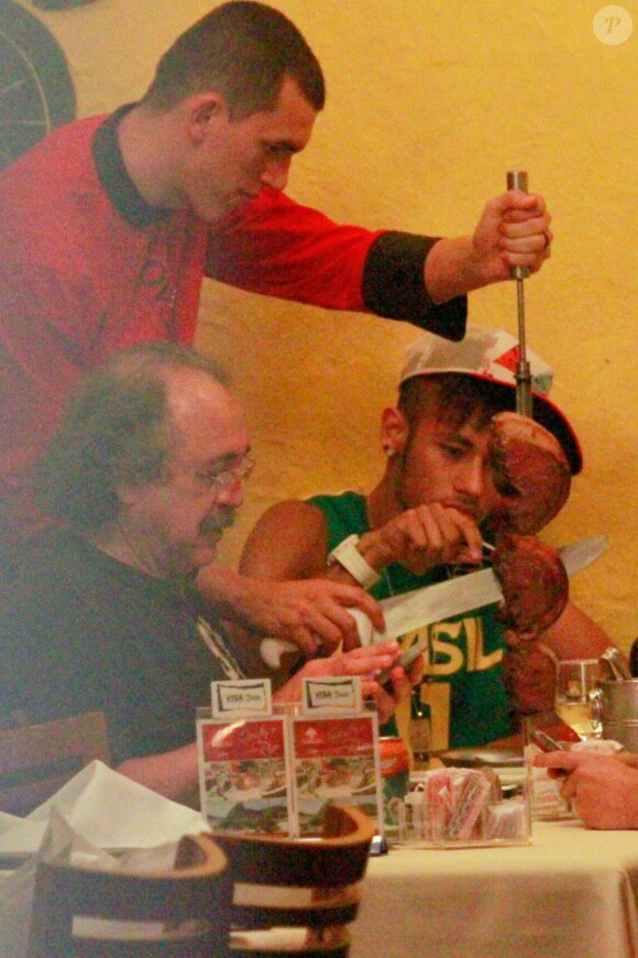 Le nouveau joueur du FC Barcelone Neymar s'offre un morceau de viande lors d'un dîner au restaurant Porcao de Rio de Janeiro le 18 juillet 2013 avec ses proches et sa famille