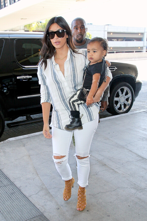 Kim Kardashian à l'aéroport de Los Angeles avec Kanye West et leur fille North, porte un chemisier rayé, un jean blanc et des sandales Hermès. Le 1er septembre 2014.