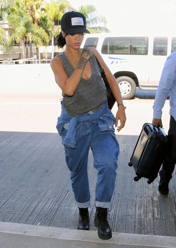 Rihanna à l'aéroport LAX de Los Angeles, porte une casquette Pigalle, un débardeur gris, une salopette Balmain (collection printemps-été 2014), un sac à dos Reece Hudson et des bottines Timberland. Le 30 septembre 2014.