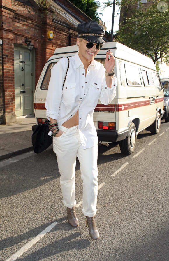 Rita Ora quitte un studio d'enregistrement à Londres, habillée d'une chemise et d'un jean blancs Levi's, et de bottines vernies. Une casquette en cuir, des lunettes Ray-Ban et un sac Chanel complètent sa tenue. Le 28 mai 2015.