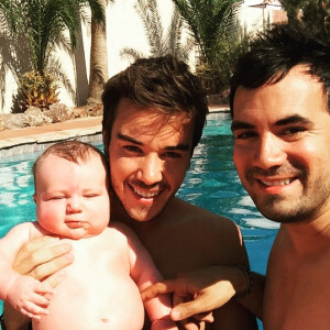 Alex Goude, Romain et leur bébé Elliot posent ensemble dans la piscine. Juin 2015.