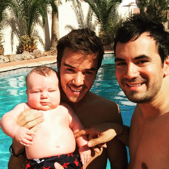 Alex Goude, Romain et leur bébé Elliot posent ensemble dans la piscine. Juin 2015.