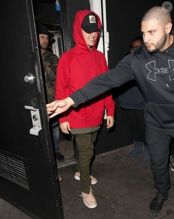 Justin Bieber quitte le Club "Nice Guy" de West Hollywood, souriant avec un sweat rouge à capuche le 15 décembre 2015.