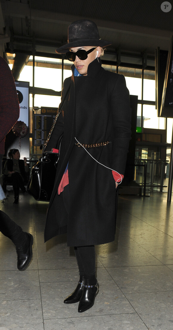 Rita Ora, toute de noir vêtue à l'aéroport d'Heathrow, porte un manteau Victoria Beckham (collection automne-hiver 2014) et des bottines Saint Laurent. Londres, le 17 mars 2016.