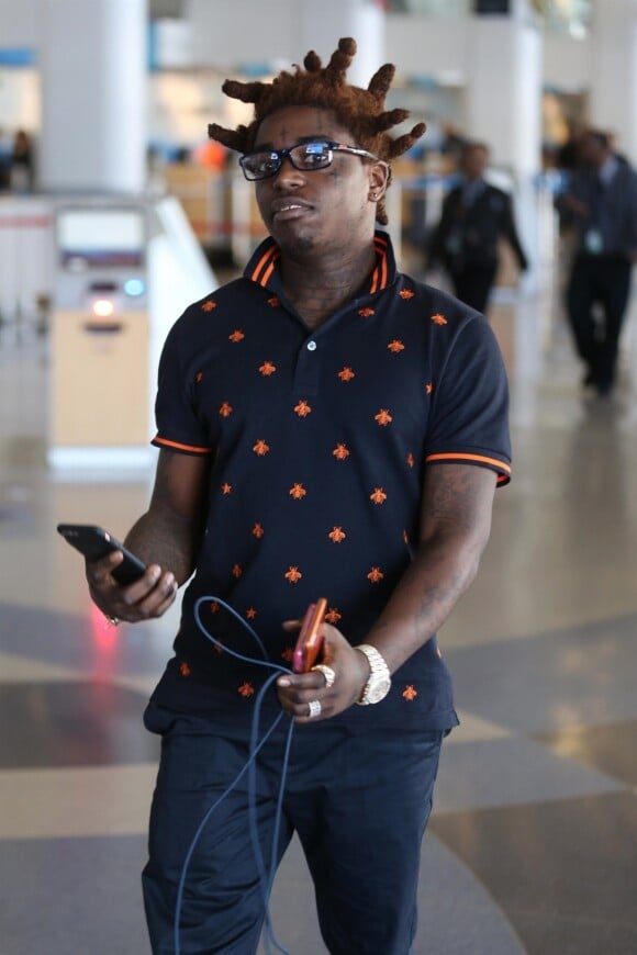 Kodak Black s'apprête à s'envoler de l'aéroport LAX à Los Angeles. Le rappeur porte un polo Gucci, un pantalon bleu marine et des mocassins Gucci orange. Il tient en main deux Iphone, le 12 décembre 2017.