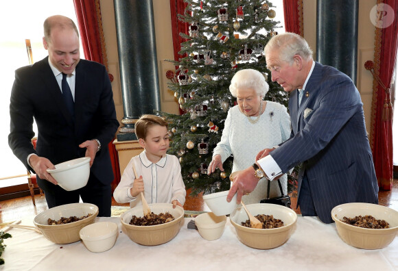 Le prince George de Cambridge prépare, sous le regard bienveillant du prince William, duc de Cambridge, du prince Charles, prince de Galles et de la reine Elisabeth II, des puddings de Noël, dans le cadre du lancement de l'initiative 'Together at Christmas' de la Royal British Legion au Palais de Buckingham, le 21 décembre 2019.