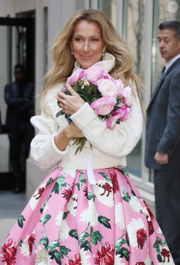 Celine Dion rayonnante et très souriante dans un ensemble pull écru et jupe bouffante fleurie salue ses fans à la sortie de son hôtel à New York, le 8 mars 2020.
