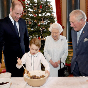 Le prince George de Cambridge prépare, sous le regard bienveillant du prince William, duc de Cambridge, du prince Charles, prince de Galles et de la reine Elisabeth II, des puddings de Noël, dans le cadre du lancement de l'initiative 'Together at Christmas' de la Royal British Legion au Palais de Buckingham, le 21 décembre 2019.