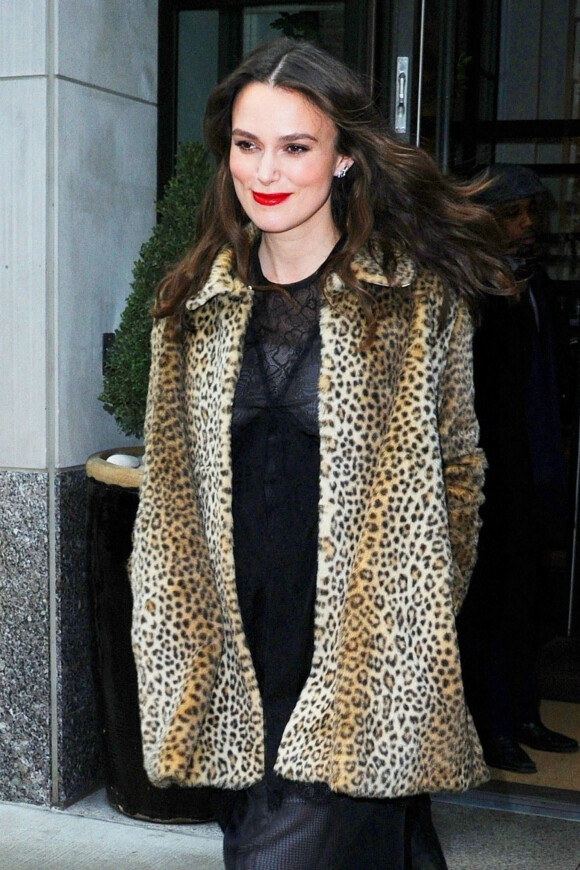 Keira Knightley glamour et souriante arrive aux studio AOL pour la promotion du film The Aftermath, elle porte un manteau de fourrure léopard, des escarpins ouverts et une longue robe en dentelle et mousseline noire, New York le 12 mars 2019.
