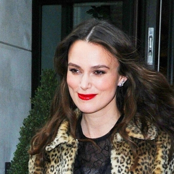 Keira Knightley glamour et souriante arrive aux studio AOL pour la promotion du film The Aftermath, elle porte un manteau de fourrure léopard, des escarpins ouverts et une longue robe en dentelle et mousseline noire, New York le 12 mars 2019.