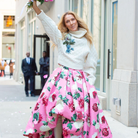 Celine Dion rayonnante et très souriante dans un ensemble pull écru et jupe bouffante fleurie salue ses fans à la sortie de son hôtel à New York, le 8 mars 2020 