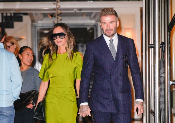 Victoria et David Beckham se tiennent la main à la sortie de leur hôtel à New York le 14 octobre 2022. Victoria porte une robe verte électrique et David un costume bleu marine.