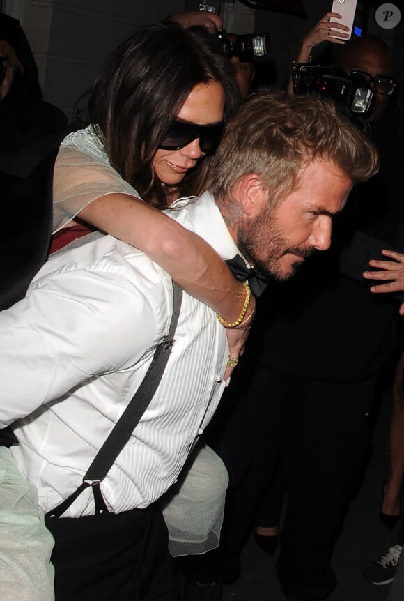 David Beckham porte sa femme Victoria Beckham sur son dos, à la sortie de la soirée de son 50ème anniversaire au club Oswald's à Londres, le 20 avril 2024