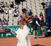 Elle est arrivée sur le court vêtue de son ensemble Nike beige à sequins, agrémenté cette fois-ci d'une longue traîne blanche.

Naomi Osaka arrive avec une traine blanche pour son second tour aux internationaux de France de Tennis de Roland Garros 2026, à Paris, France, le 28 mai 2026. © Imago/PsnewZ/Bestimage
