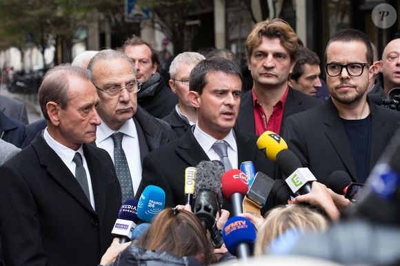 Le ministre de l'Intérieur Manuel Valls s'adresse à la presse en compagnie du directeur de Libération Fabrice Rousselot (au centre, chemise rouge), du président de Libération Nicolas Demorand (à droite) et du maire de Paris Bertrand Delanoë (à gauche) devant le siège du quotidien français Libération, le 18 novembre 2013 à Paris, France. Un tireur a ouvert le feu dans le hall du bâtiment, blessant un photographe débutant. Photo par Romain Boe/ABACAPRESS.COM