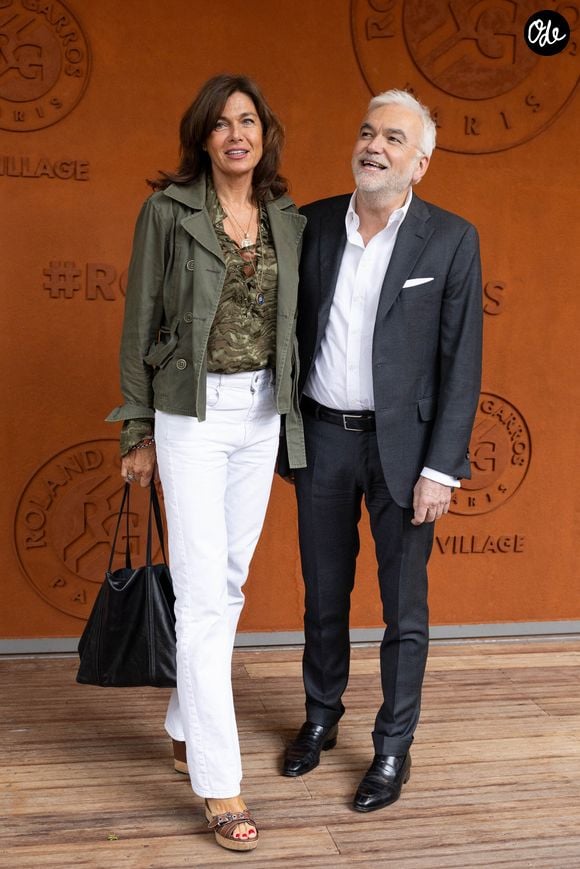 L'animateur de CNews, Pascal Praud, a pris la pose dans un élégant costume gris au bras de sa compagne Catherine, vêtue d'une veste vert kaki.

Pascal Praud et sa compagne Catherine Bancarel au photocall du village lors des Internationaux de France de Tennis de Roland Garros 2026, à Paris, France, le 5 juin 2026. © Jacovides-Moreau/Bestimage