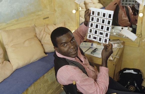 Exclusif - En France, à Paris, portrait en intérieur de Jacques Martial dans sa loge du théâtre de la Gaité-Montparnasse, assis, tenant une planche de diapositives, vêtu d'un jean, d'une chemise rose et d'un gilet gris. 1990
© Alain Canu via Bestimage