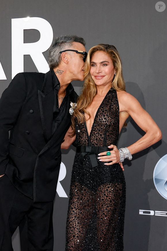 Le chanteur britannique portait un costume croisé noir avec une imposante broche, tandis que la mère de ses quatre enfants arborait une longue robe noire transparente à sequins.

Robbie Williams et sa femme Ayda Field - Photocall du gala " amfAR 2026 by Chopard " à l'Hôtel du Cap-Eden-Roc à Antibes, lors du 79ème Festival International du Film de Cannes. Le 21 mai 2026
© Jacovides-Moreau / Bestimage