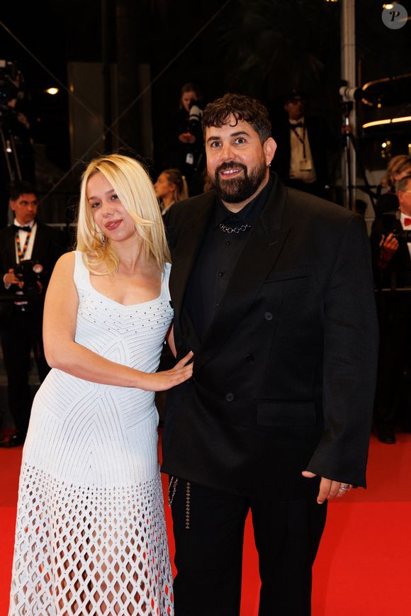 À ses côtés, Artus a prouvé qu'il maîtrisait les codes de l'élégance cannoise avec une touche de modernité bien à lui. L'acteur et humoriste avait opté pour un total look noir résolument pointu : un costume croisé oversize au tombé impeccable, associé à une chemise noire boutonnée jusqu'au col.

Artus et sa compagne Kim Higelin - Montée des marches du film "Jim Queen" lors du 79ème Festival International du Film de Cannes le 18 mai 2026.

© Moreau / Jacovides / Bestimage