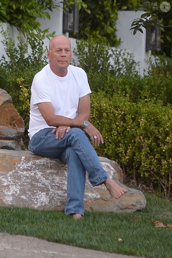 Exclusif - Bruce Willis est assis pieds nus sur un rocher et regarde passer les voitures sur Sunset Boulevard à Los Angeles, le 22 septembre 2019. Il porte un jean et un t-shirt blanc.